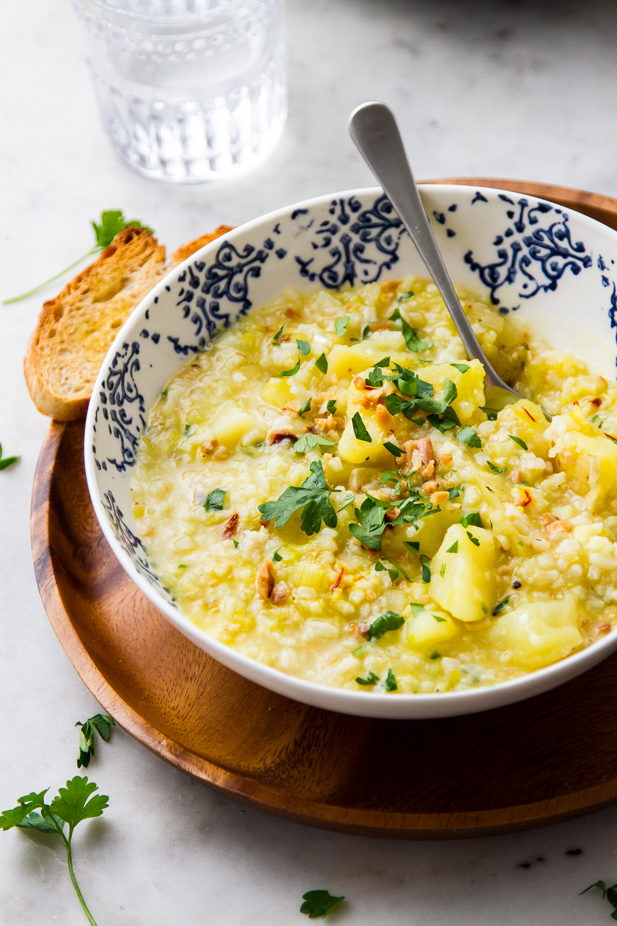 side view of cozy bowl of rustic potato leek soup with rice, fried garlic and almonds with parsely.