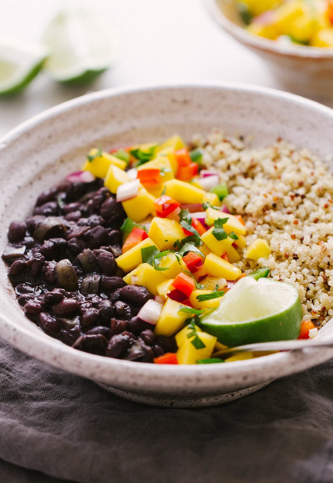 side view of cuban black bean bowl with quinoa and mango salad with lime wedges.