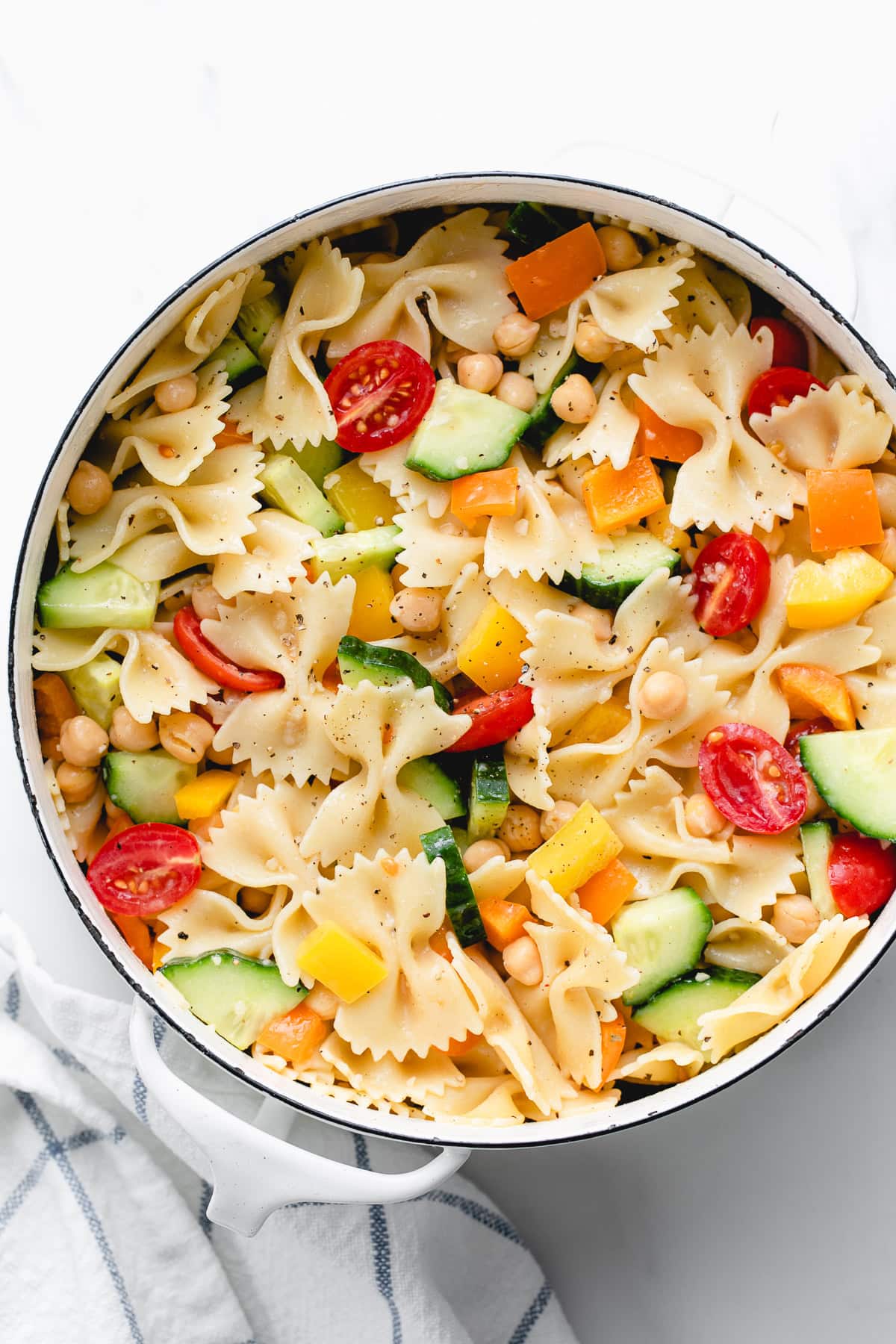 top-down shot of a beautiful pasta salad bowl with colorful pasta, cherry tomatoes, cucumber, red onion, bell peppers, chickpeas and a light dressing drizzle.