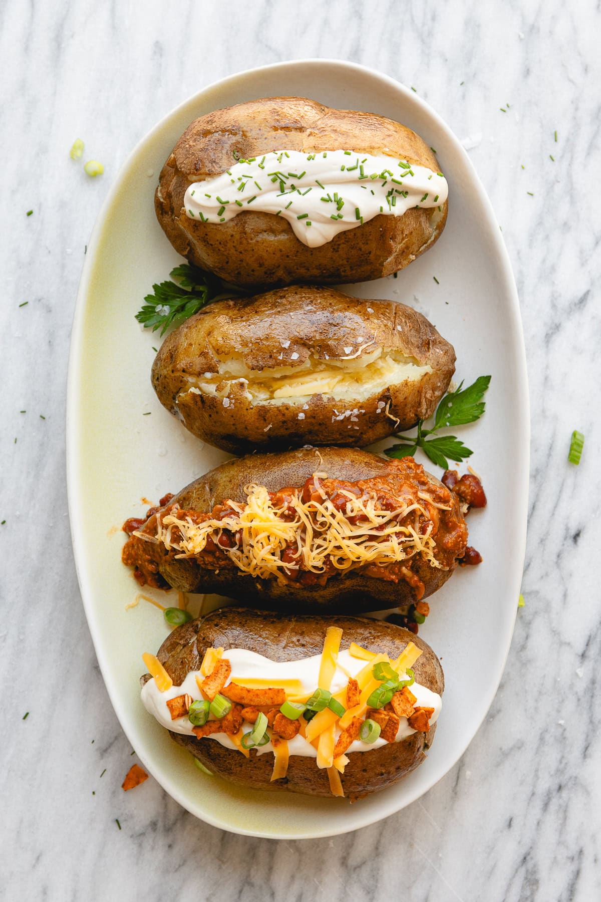 top down view of variety of baked potatoes on a serving plate, each with different toppings.