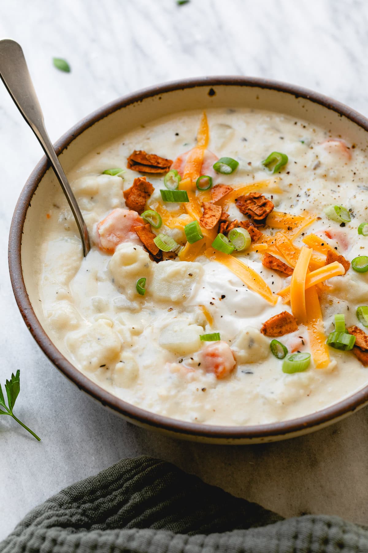 side angle view of bowl of vegan potato soup with topping and spoon.