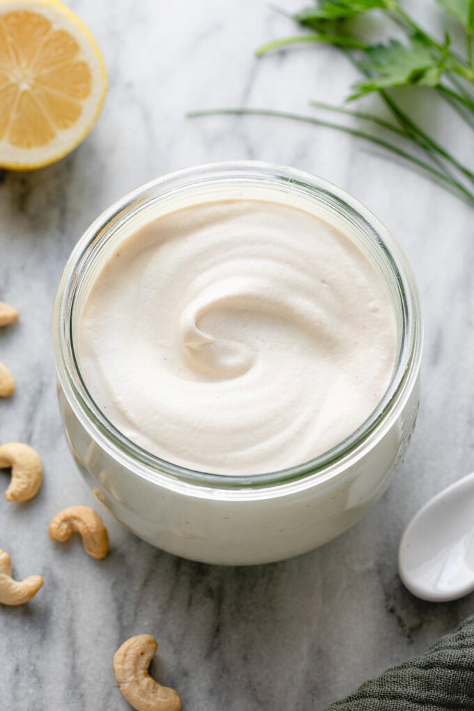 side angle view of vegan sour cream in a glass container with items surrounding.