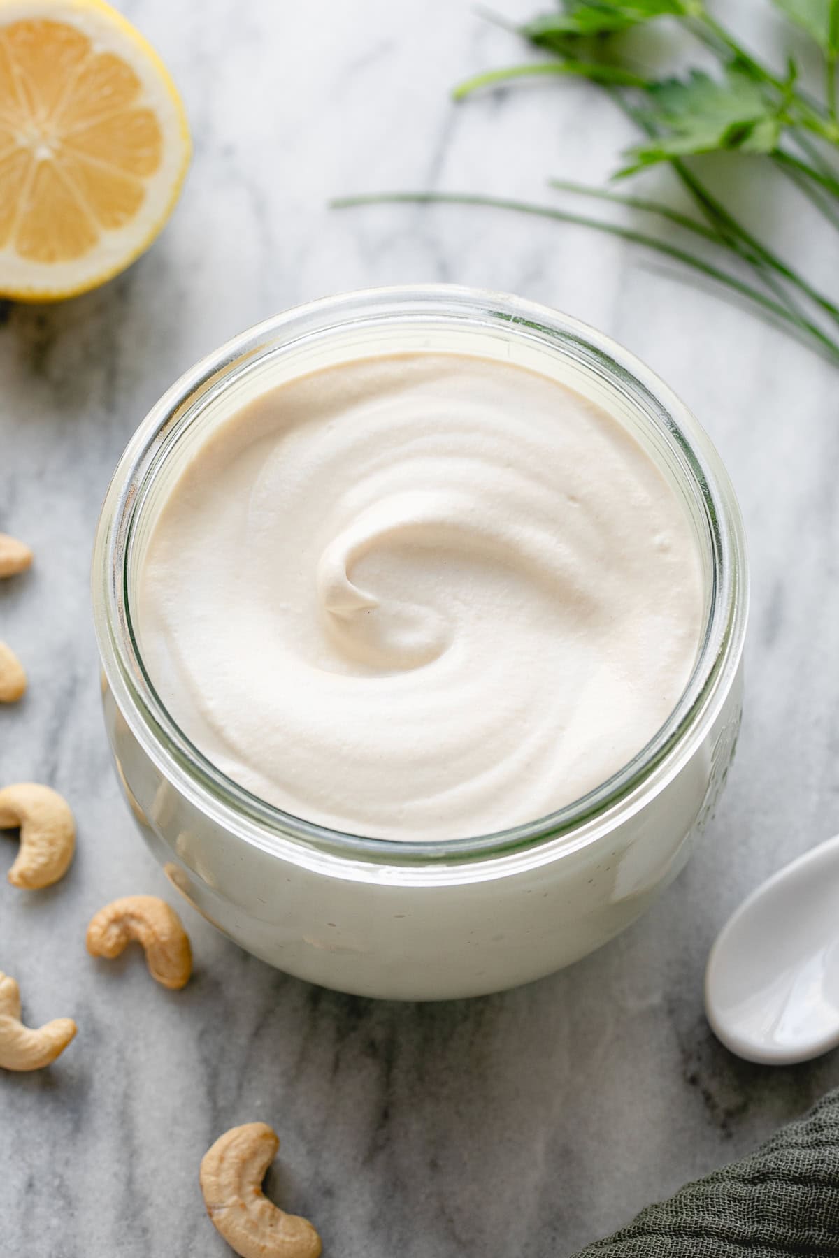 side angle view of vegan sour cream in a glass container with items surrounding.
