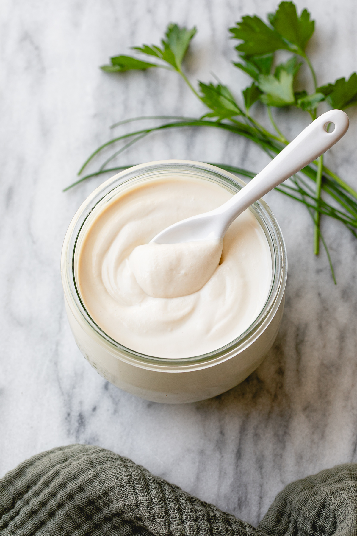 side angle view of diary-free sour cream in a glass jar with spoon and items surrounding.