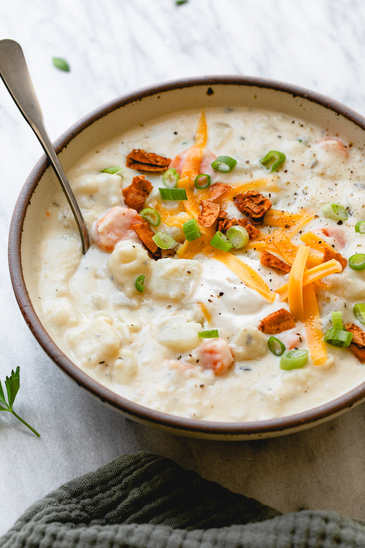 side angle view of bowl of vegan potato soup with topping and spoon.