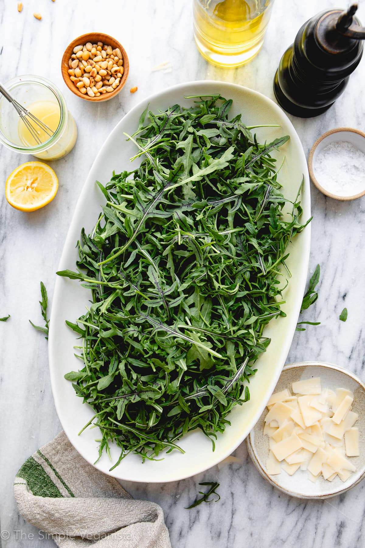 Fresh arugula salad with lemon, olive oil, and toppings on a white platter.