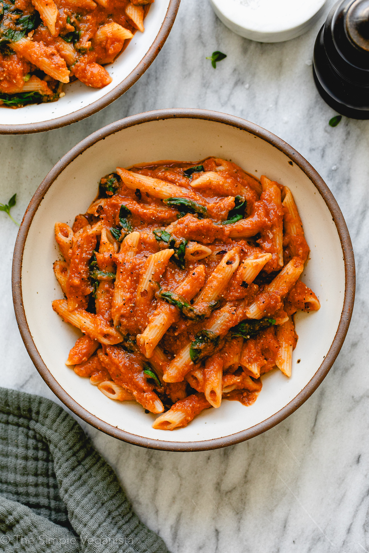 top down view of plated red lentil pasta sauce with penne and spinach, and items surrounding.