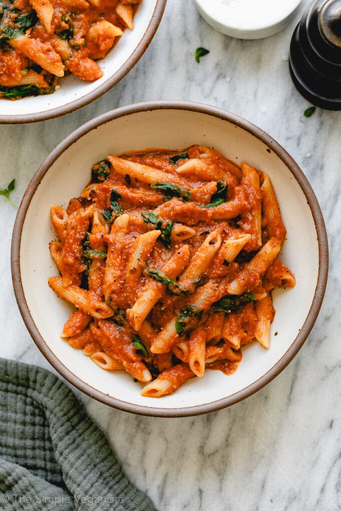 top down view of plated red lentil pasta sauce with penne and spinach, and items surrounding.