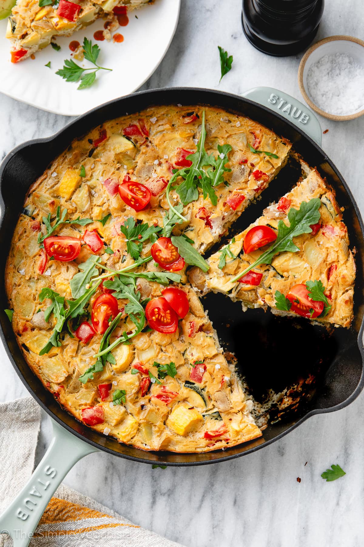 top down view of vegan frittata in a pan with slices cut and items surrounding.