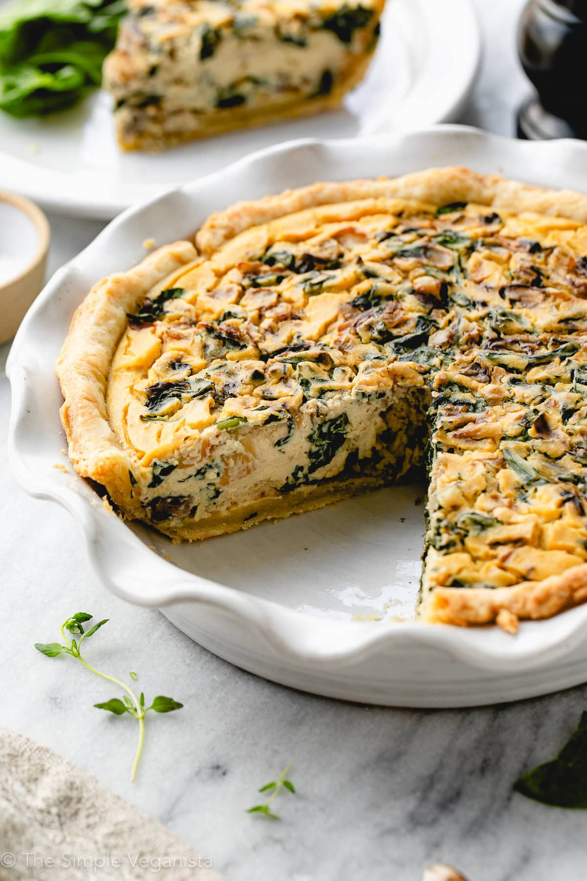 side angle view of tofu-based quiche in a pie dish with slice of plate behind it.