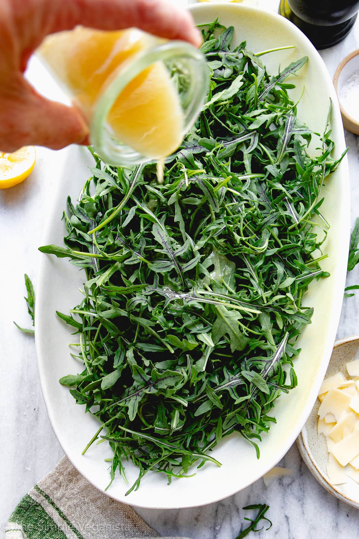 top down view of arugula salad with lemon dressing being poured over top on a white platter.
