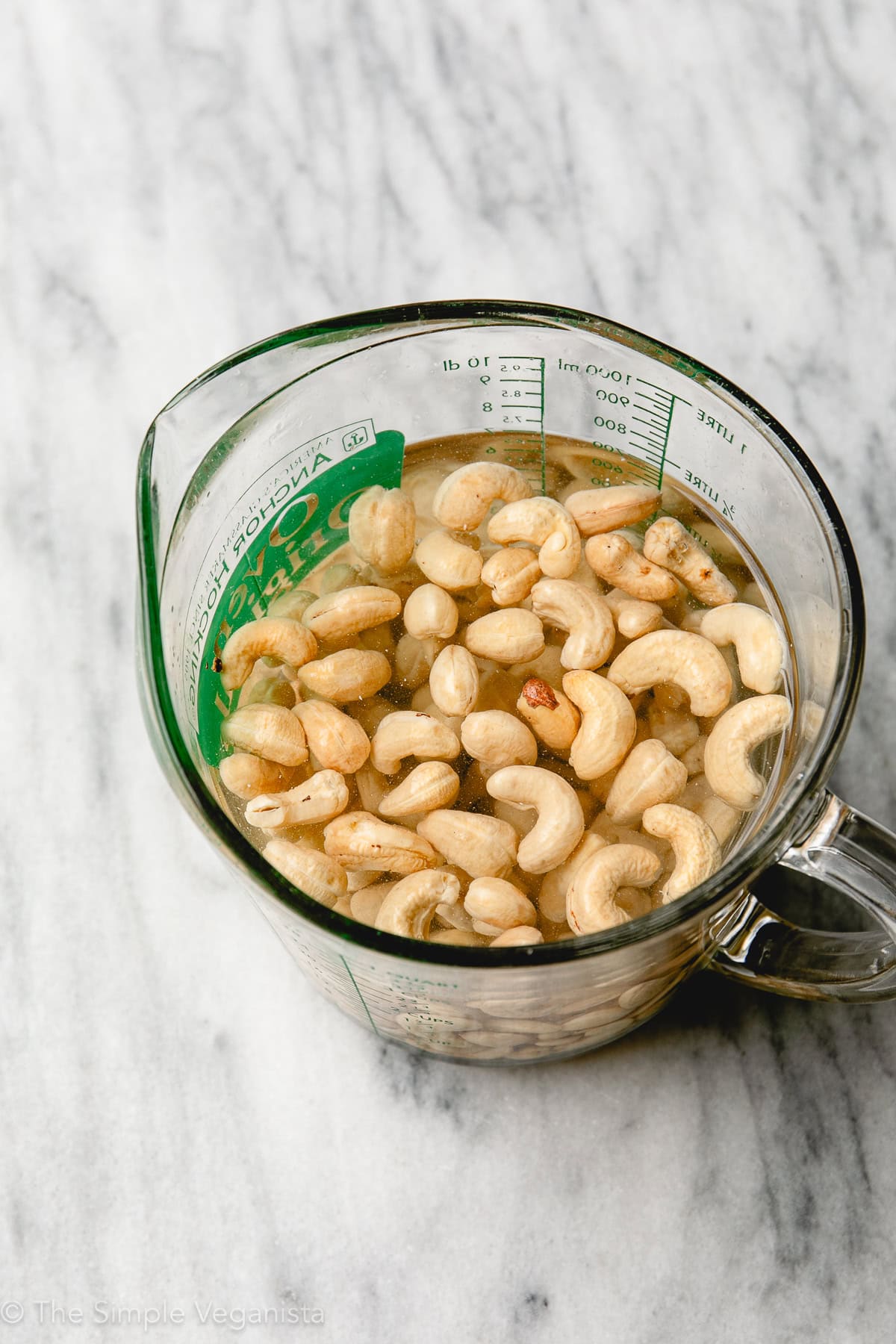 raw cashews soaking in a glass measuring cup with water.