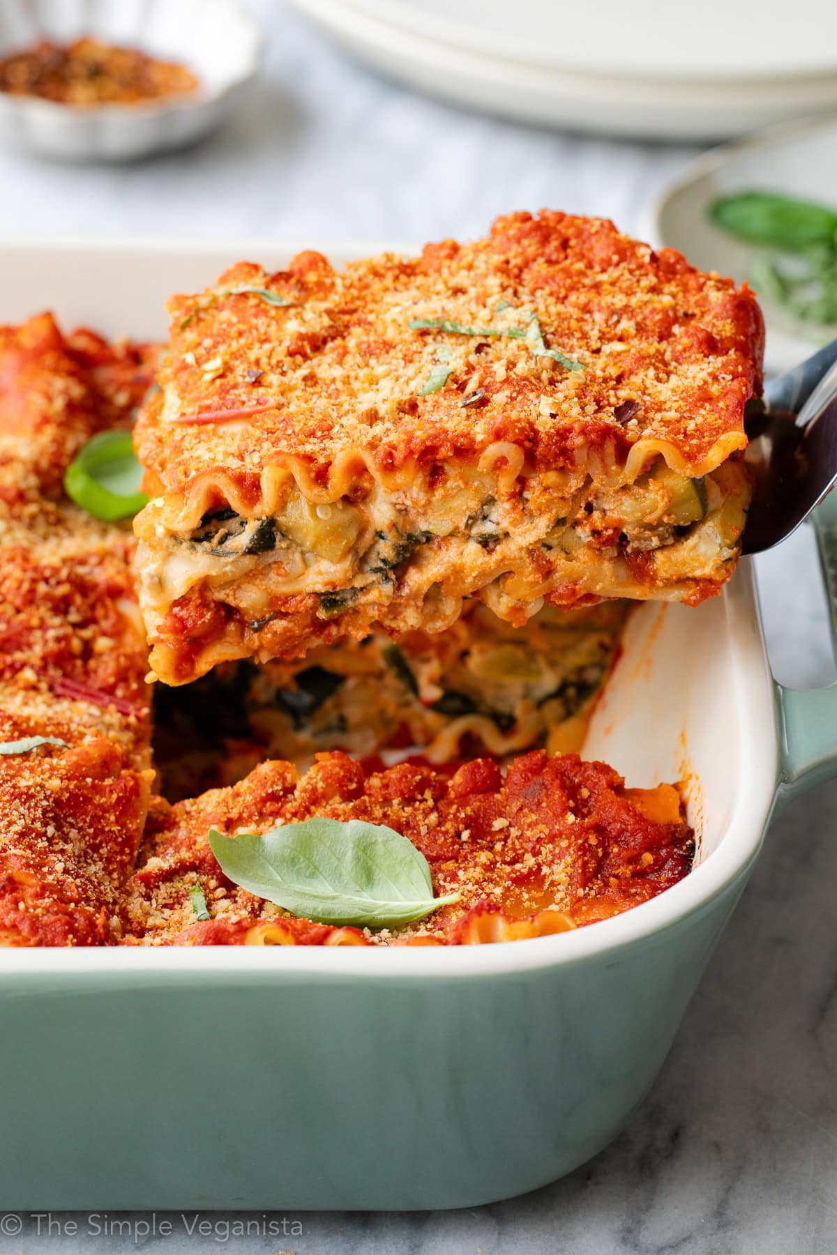 side angle view of a hearty slice of vegan lasagna served in a baking dish, garnished with fresh basil leaves.