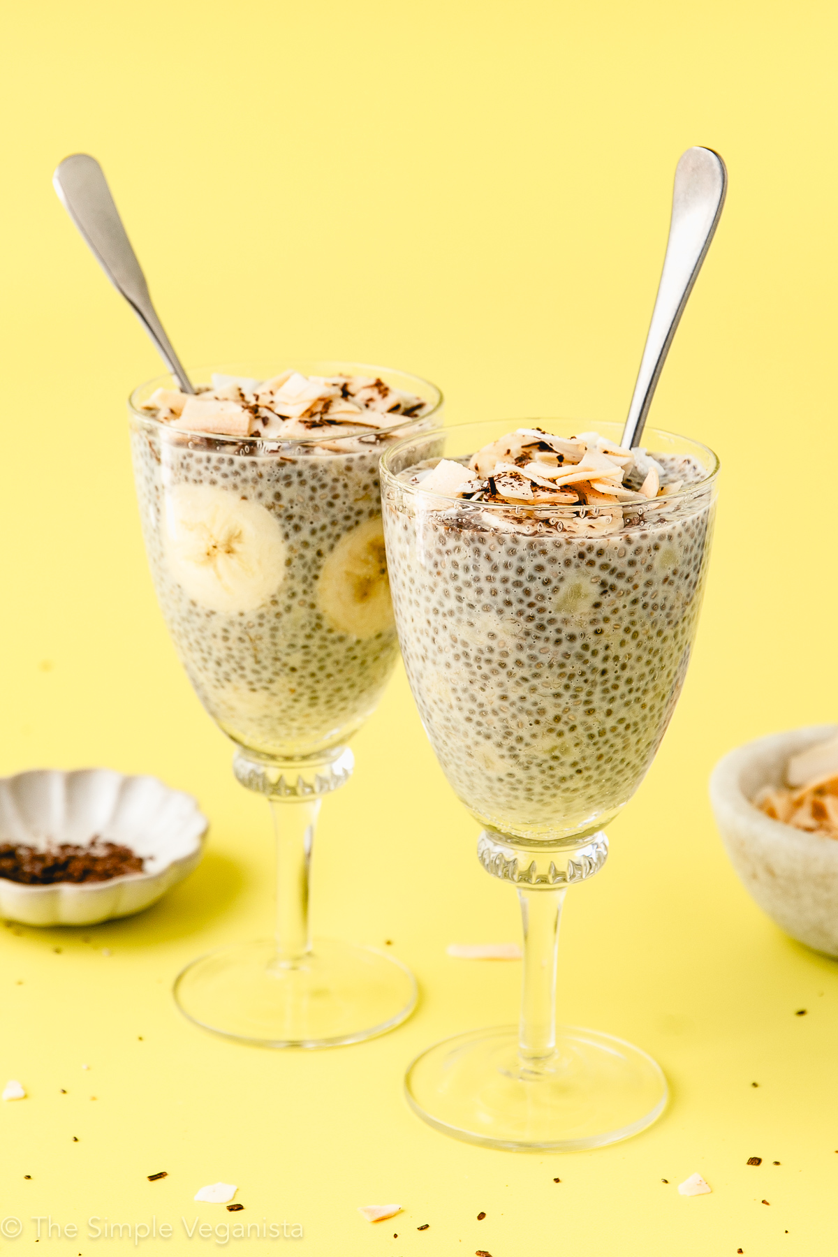 head on view of banana chia pudding in glasses ready to serve with toppings and items surrounding.