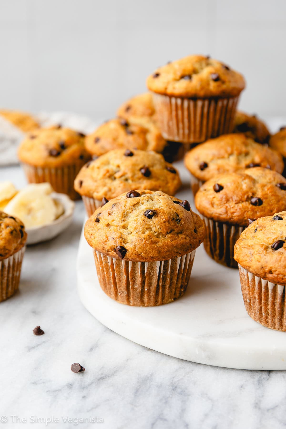 head on view of group of banana muffins with chocolate chips on a marble slab with other items surrounding.