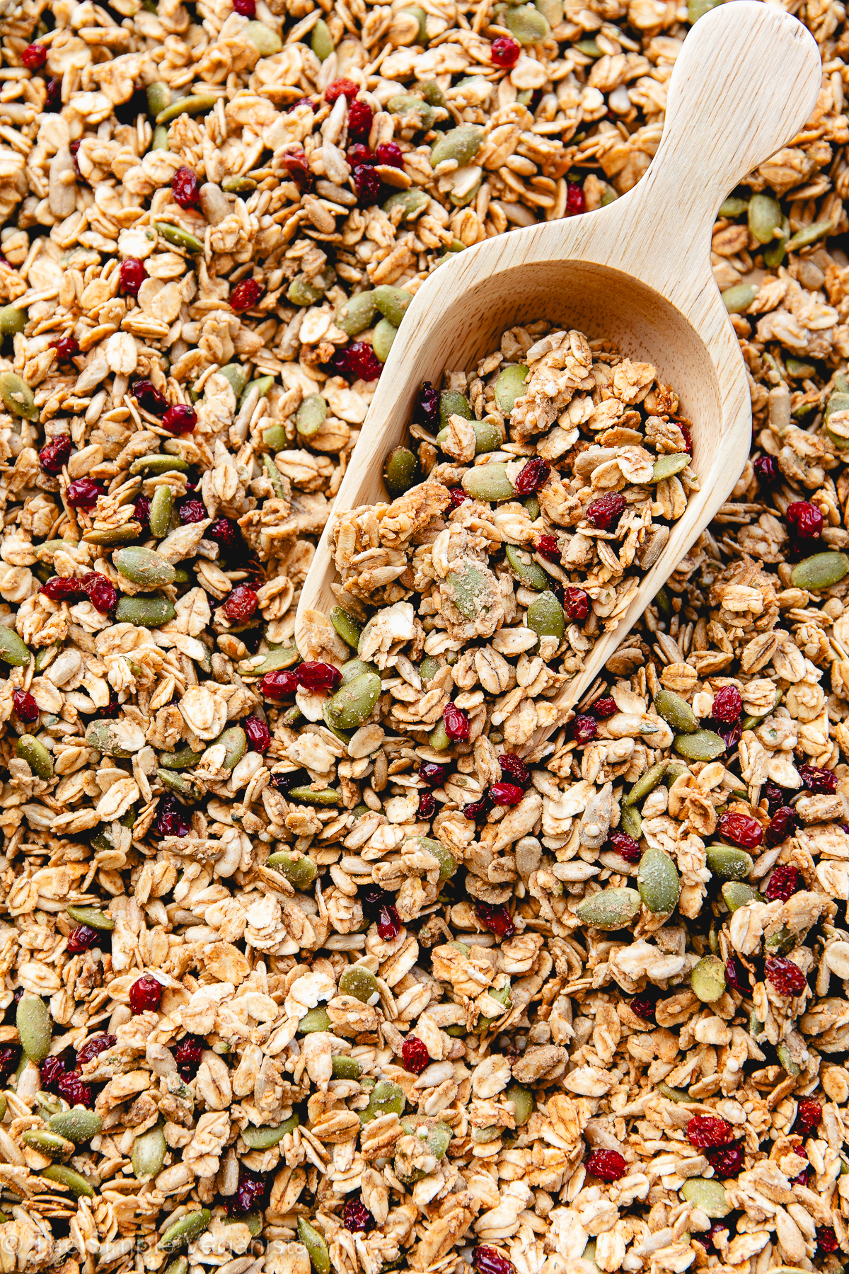 side angle view of freshly made granola on a rimmed baking sheet with wooden scoop.