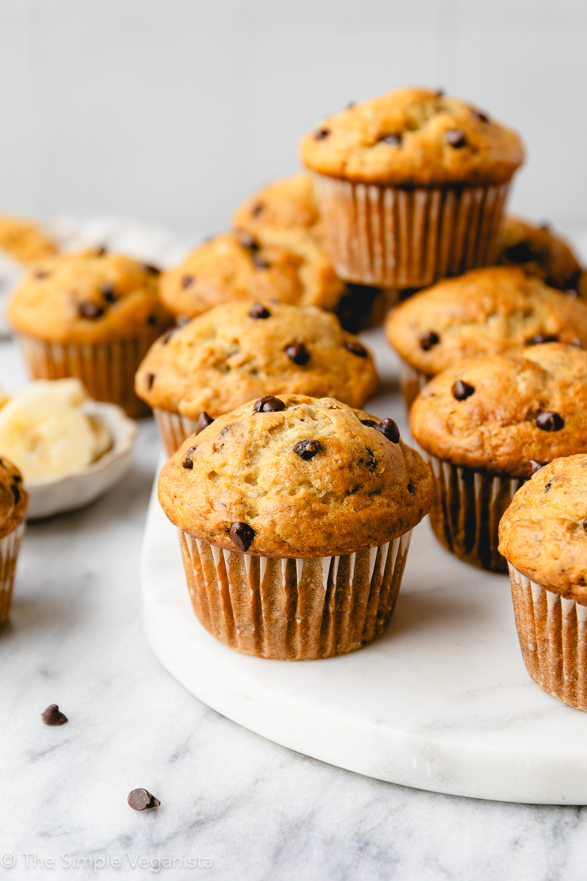 head on view of group of banana muffins with chocolate chips on a marble slab with other items surrounding.