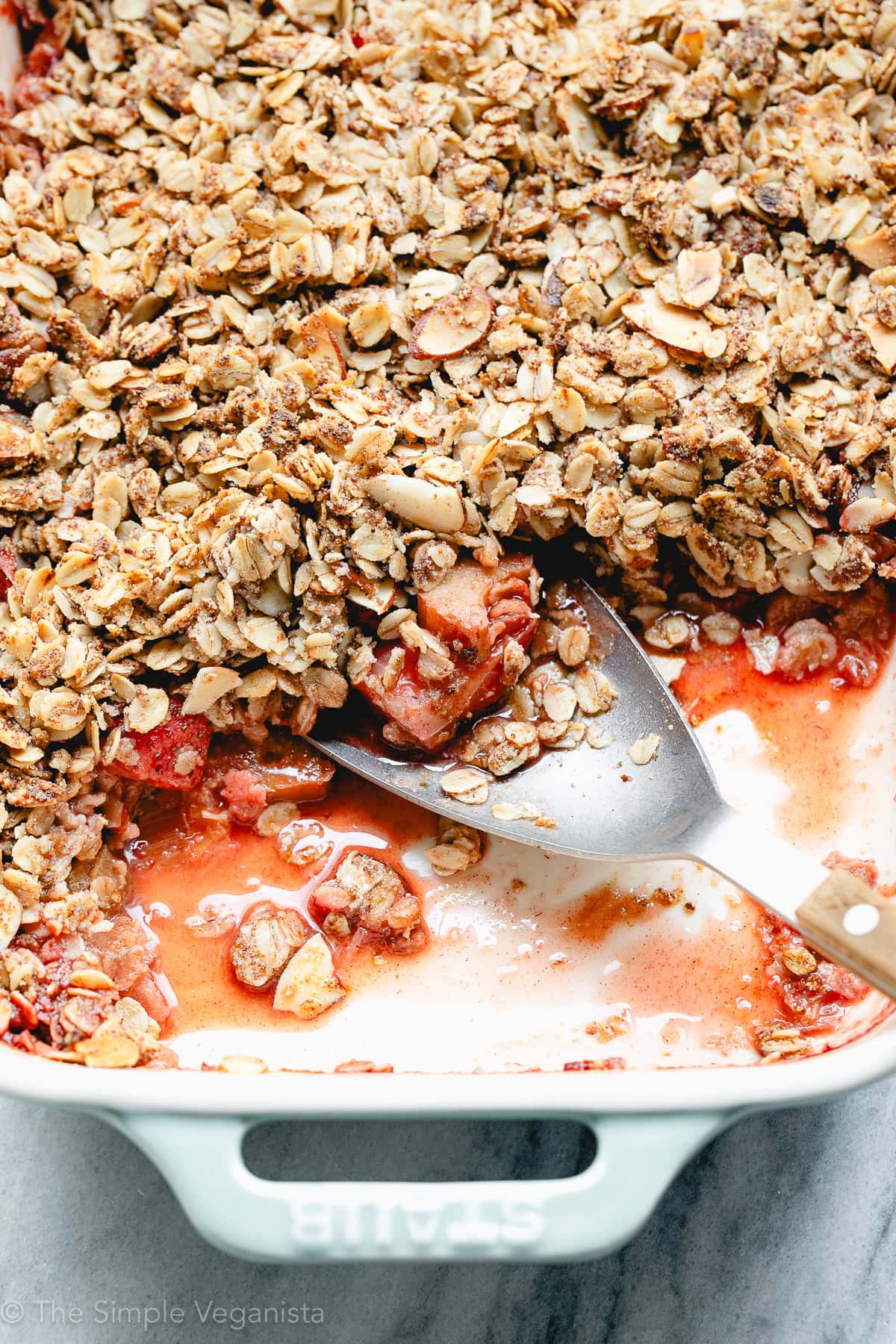 side angle view of strawberry rhubarb crisp in a baking dish with serving spoon.