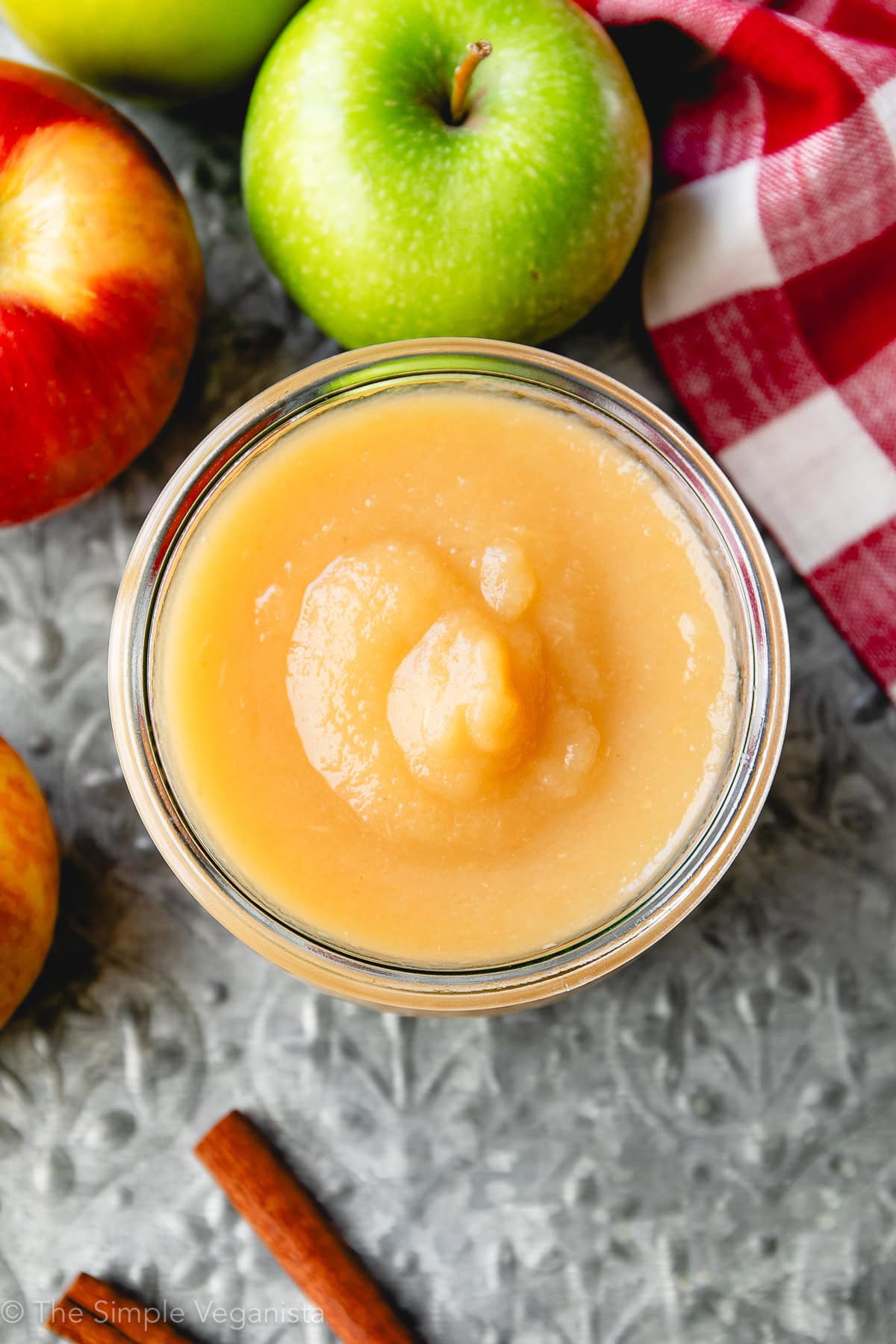 top down view of homemade applesauce in glass jar with fresh apples surrounding.