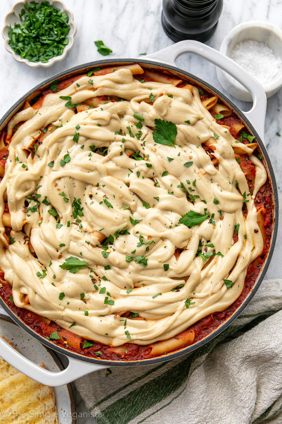 Top down view of vegan baked ziti in a white baking dish with melted cashew ricotta and fresh parsley.